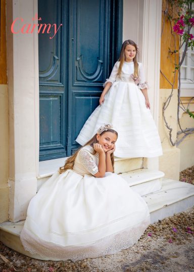 Comunión niña Dos niñas en vestidos de fiesta blancos, una sentada y otra de pie en una escalera.
